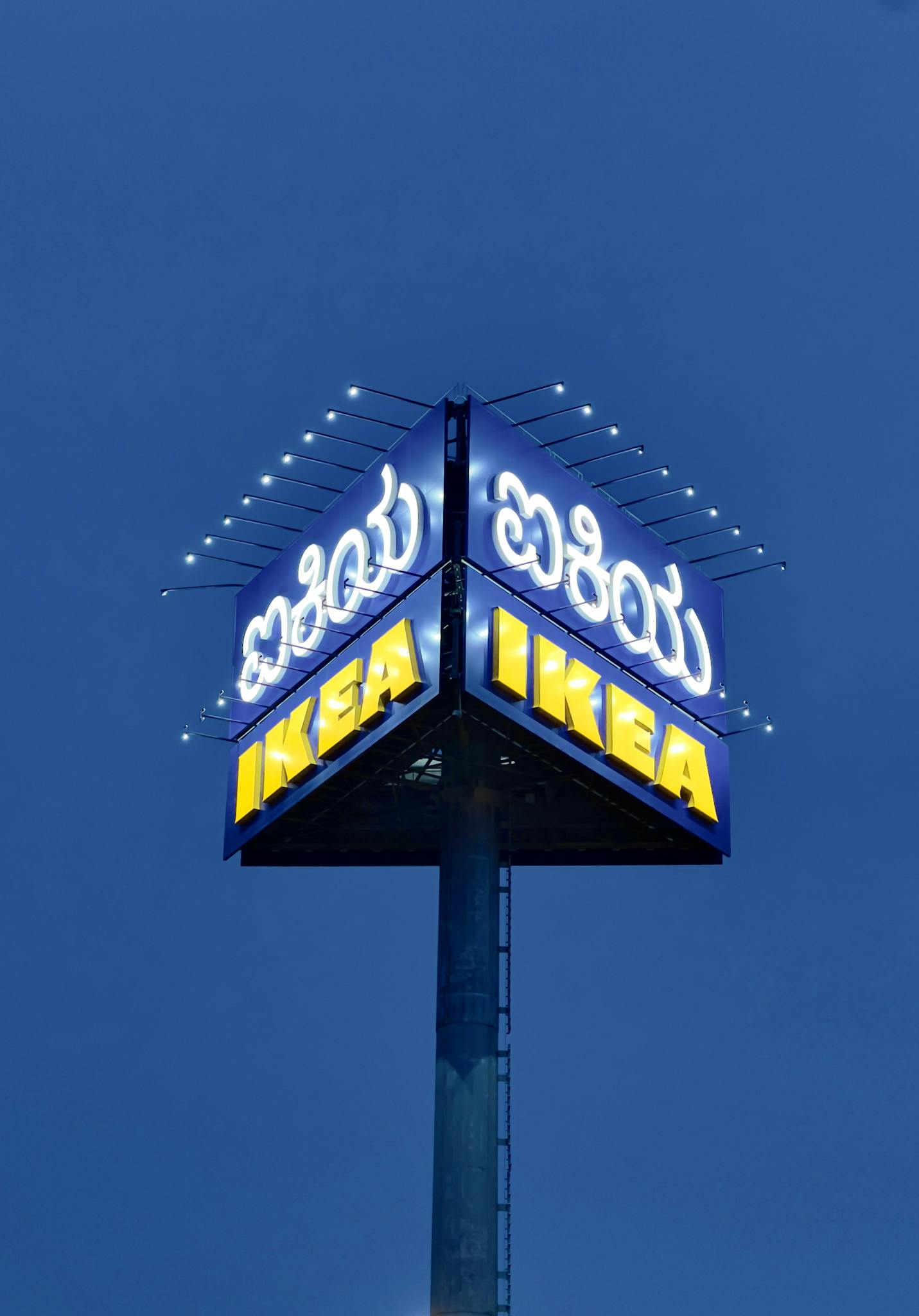 A glowing IKEA sign stands tall against a clear night sky, illuminating the surroundings.